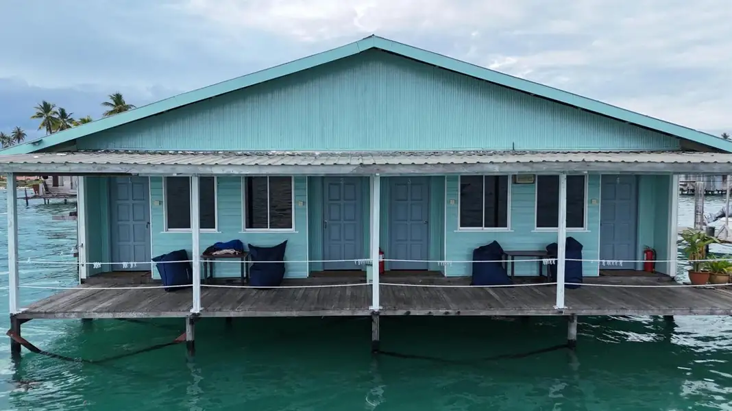 A long light-blue overwater bungalow featuring a continuous wooden deck with blue bean bags and multiple room entrances at Bigfin Water Bungalow.