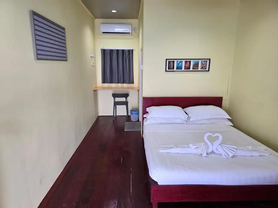 A cozy double bedroom at Bigfin Water Bungalow near Pulau Bum Bum featuring a large bed, traditional style furniture, dark wooden floors, and AC.
