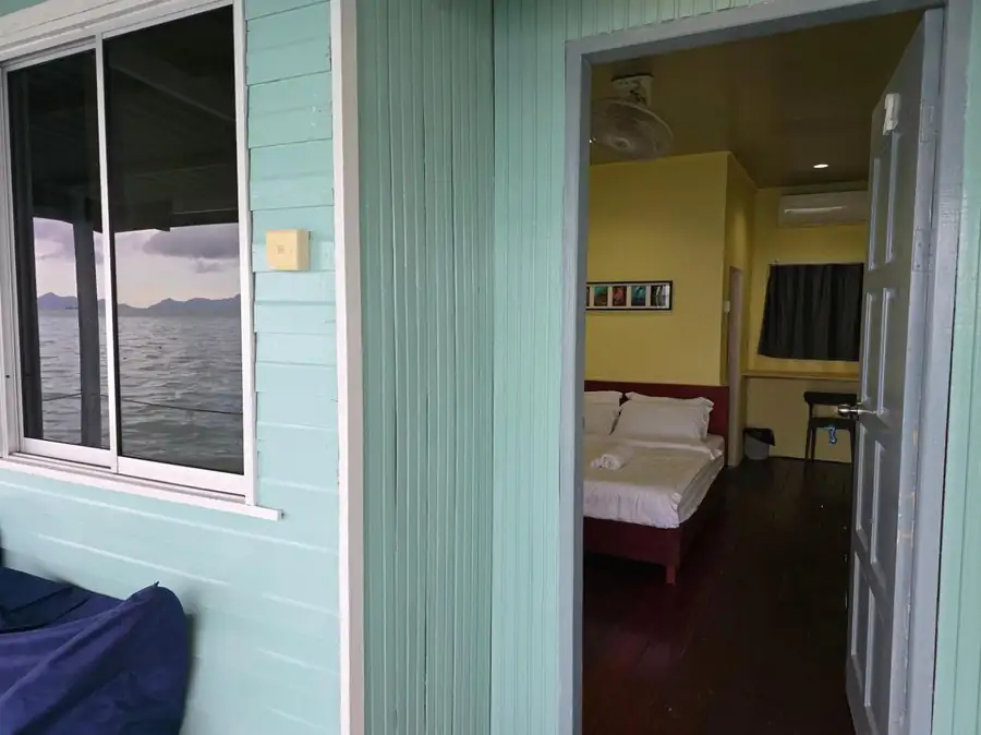 An inviting bedroom at Bigfin Water Bungalow near Pulau Bum Bum featuring a large bed, traditional style furnishings, sleek timber floors, air con, and a window framing the ocean.