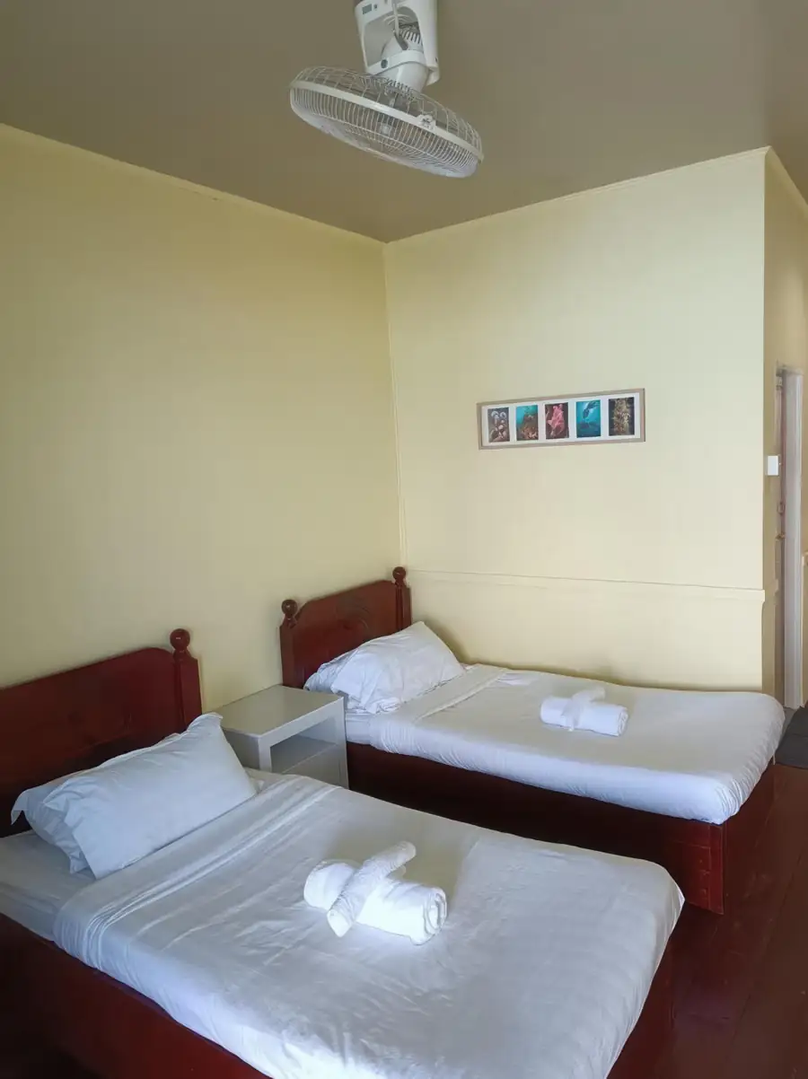 A simple twin bedroom at Bigfin Water Bungalow in the Tun Sakaran Marine Park offering two comfortable beds, traditional style wooden headboards, dark wooden floors, and A/C.